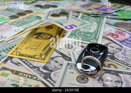 A car key on the background of various currency notes and one symbolic gold dollar banknote. Concept of the cost of purchasing, renting and maintainin Stock Photo