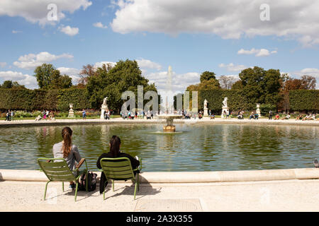 Two young women sitting by the Grand Bassin Rond pond with fountain in the Tuileries garden on a summer day in Paris, France. Stock Photo
