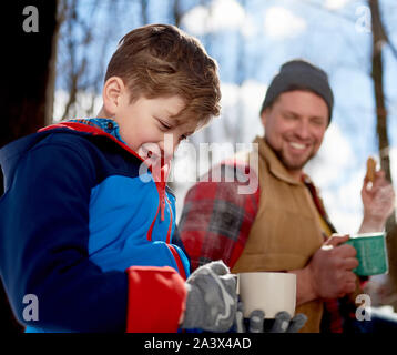 Family of a mother, father and boy child having fun and sharing a cup of cocoa and chocolate chip cookies in snow during the winter season Stock Photo