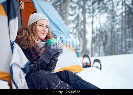 Millenial blond girl setting camp with a tent in a snow filles canadian park during a snowshoeing trip Stock Photo