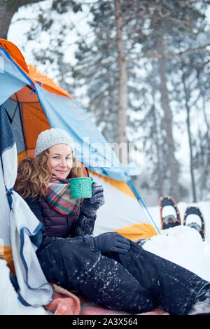 Millenial blond girl setting camp with a tent in a snow filles canadian park during a snowshoeing trip Stock Photo