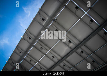 Solar photovoltaic panels, conduits, and wires collect power against blue sky. Stock Photo