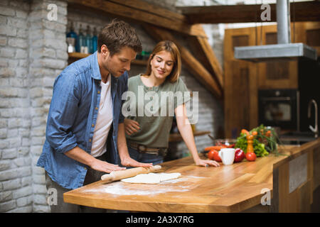 Cheerful young couple making pizza in rustic kitchen together Stock Photo