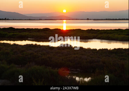 sun setting behind mountains and reflecting in ebro river and sea in ebro delta national park in catalunya, spain, with warm colors Stock Photo