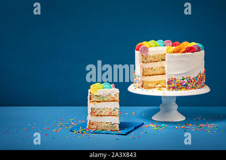 Sliced confetti Birthday cake  with rainbow colored icing and Sprinkles over a blue background. Stock Photo