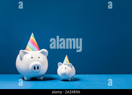 Piggy Banks wearing birthday hats over a blue background. Birthday Money Concept. Stock Photo