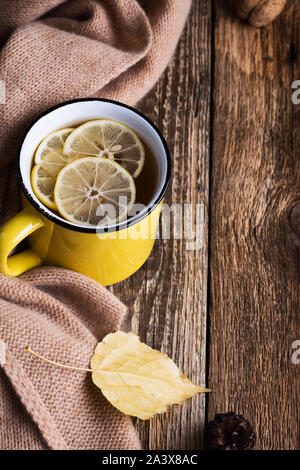 Hot tea in yellow mug and fresh lemon on wooden table, autumn tea time.  Christmas  or Thanksgiving day cozy  warm hot beverage and woolen scarf, clos Stock Photo