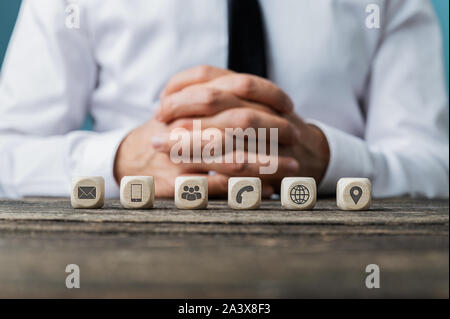 Customer service and help concept - business operator sitting at rustic wooden desk with six dices with contact and information symbols on them placed Stock Photo