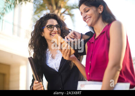 Two happy female business colleagues reviewing filed documents together outdoors in city Stock Photo