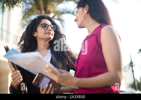Two happy female business colleagues reviewing filed documents together outdoors in city Stock Photo