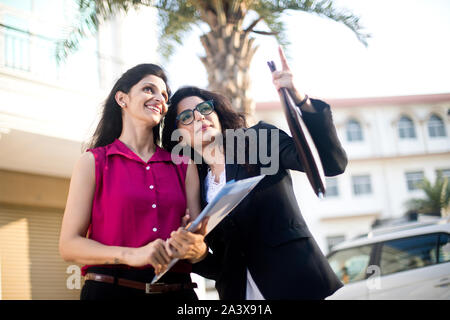 Two happy female business colleagues reviewing filed documents together outdoors in city Stock Photo