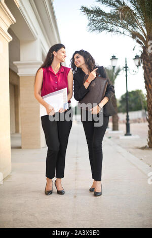 Two happy female business colleagues reviewing filed documents together outdoors in city Stock Photo
