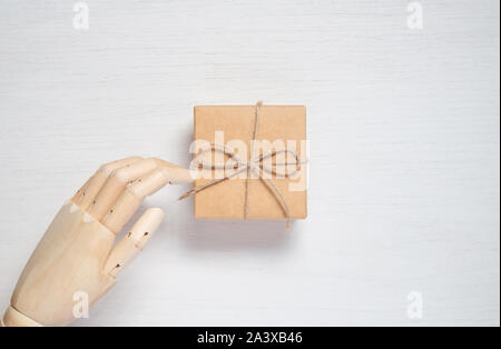 Wooden mannequin hand opens a gift in a box tied with twine. Gift background concept for holiday makers. Greeting card for christmas, birthday and new Stock Photo