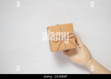 Wooden mannequin hand opens a gift in a box tied with twine. Gift background concept for holiday makers. Greeting card for christmas, birthday and new Stock Photo