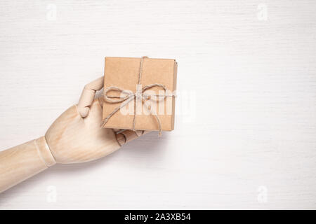 Wooden mannequin hand opens a gift in a box tied with twine. Gift background concept for holiday makers. Greeting card for christmas, birthday and new Stock Photo