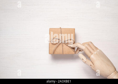 Wooden mannequin hand opens a gift in a box tied with twine. Gift background concept for holiday makers. Greeting card for christmas, birthday and new Stock Photo