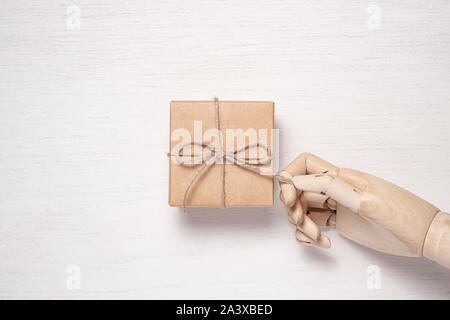 Wooden mannequin hand opens a gift in a box tied with twine. Gift background concept for holiday makers. Greeting card for christmas, birthday and new Stock Photo