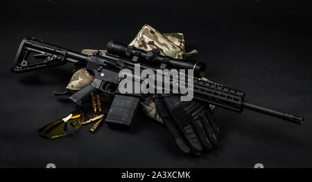 Modern automatic carbine with a telescopic sight on a dark background. Weapons for aimed shooting at long distances. Gloves ammo and glasses near the Stock Photo