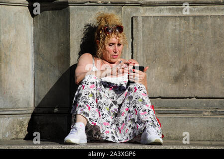 Woman using smartphone on the steps of Fontana di Santa Maria in Trastevere in Rome, Italy Stock Photo