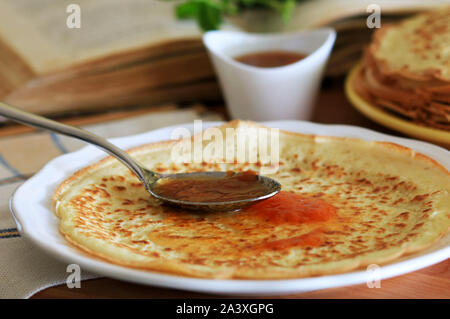 Close-up of fresh homemade crepe on white plate and strawberries marmalade with spoon Stock Photo