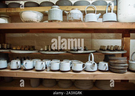 Handmade ceramic pottery in a potter's workshop. Clay plates, mugs and teapots on the shelves in the workshop studio. Stock Photo
