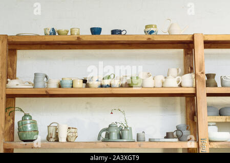 Handmade ceramic pottery in a potter's workshop. Clay plates, mugs and teapots on the shelves in the workshop studio. Stock Photo