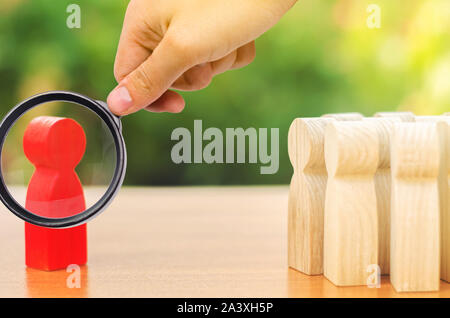 A magnifying glass looks at a red figurine of a man stands aside from the crowd of people. Asociality, sociopathy. Development of leadership and socia Stock Photo