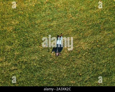 Top view of a girl lying on green grass. Photo made with a drone. Stock Photo