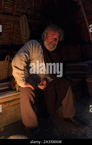 Interpreter in viking role in reconstructed village long house, lit by fire light, in L'Anse aux Meadows National Historic site on the Great Northern Stock Photo