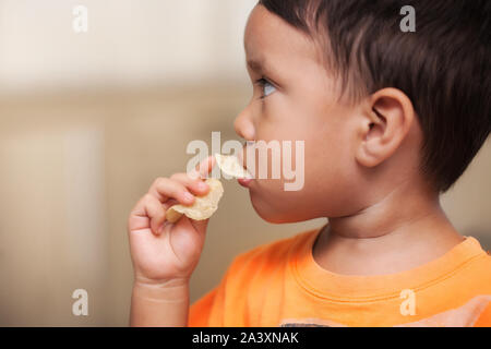 A little kid filling his mouth full of a high-fat and not very nutritious popular snack, aka; potato chips. Stock Photo