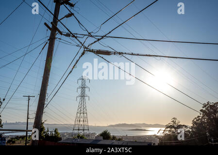 Sun shines through power lines attached to a pole framing a PG&E transformer tower with San Francisco Bay and Golden Gate Bridge in the background. Stock Photo