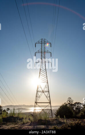 Tall PG&E transformer tower with power lines and view of San Francisco Bay from El Cerrito hills, rainbow arc and lens flare as sun shines through.