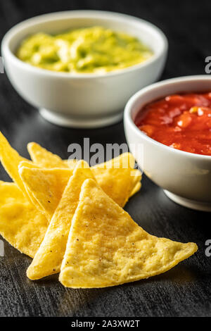 Corn nacho chips with avocado and tomato dip. Yellow tortilla chips and guacamole salsa on black table. Stock Photo