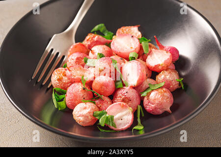 Beautiful roasted radishes in a black plate on concrete background, close up. Stock Photo