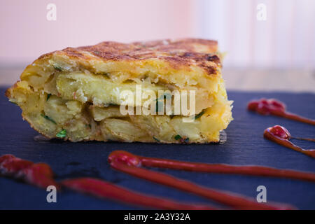 Spanish omelette with ketchup, on black surface Stock Photo