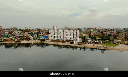 Slums in Manila near port on the bank of a river polluted with garbage, aerial view. Stock Photo