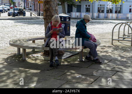 Two people sat on a bench reading Stock Photo