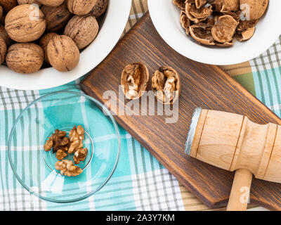 Whole walnuts, shells and kernels in a bowls around a brown wooden board with cracked nuts and wooden meat mallet. Natural unbleached Juglans regia. Stock Photo