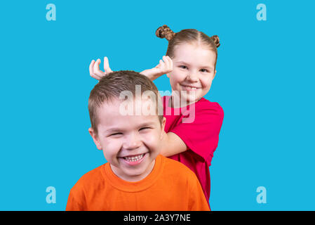 Little girl puts horns to a boy isolated on a blue background Stock Photo