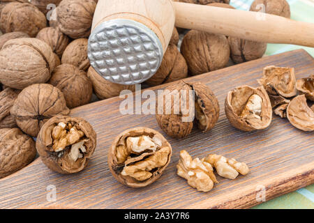 Cracked walnuts (Juglans regia) and kernels on a brown wooden board near wooden meat mallet. Natural unbleached nuts. Vegetarian food. Stock Photo