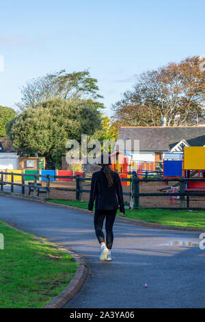 A young woman in exercise clothing walking through a park Stock Photo