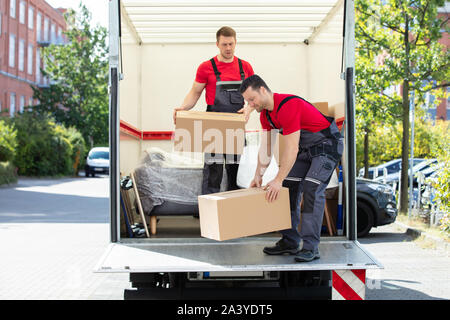 Two Young Male Mover In Uniform Unloading The Cardboard Boxes From Truck On Street Stock Photo