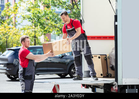 Male Movers Unloading And Passing A Cardboard Box To His Assistant In Moving Van Stock Photo