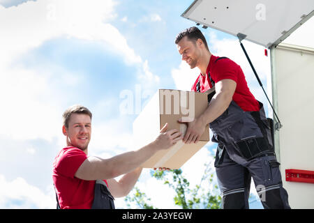 Male Movers Unloading And Passing A Cardboard Box To His Assistant In Moving Van Stock Photo