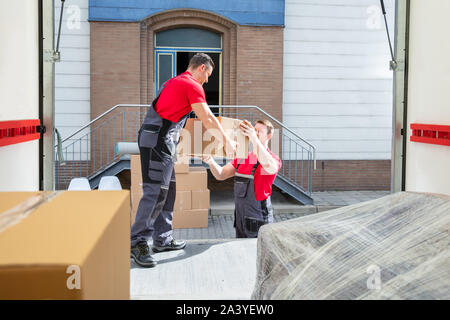Young Male Movers Unloading The Cardboard Boxes In The Van Outside The House Stock Photo