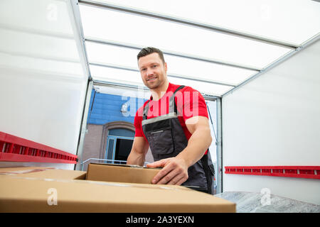 Portrait Of A Mover In Uniform Arranging The Moving Cardboard Boxes Inside The Van Stock Photo