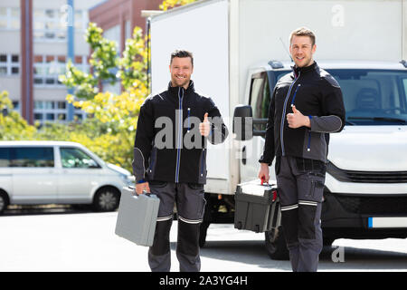 Portrait Of Two Smiling Young Male Technician Showing Thumbs Up Sign Standing Stock Photo