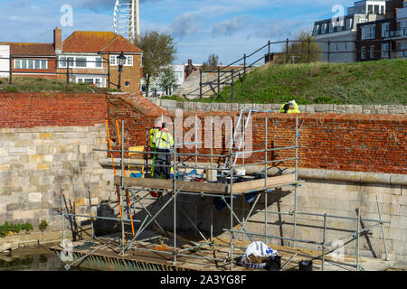 Bricklayers working on repairing a brick wall standing on scaffolding wearing harnesses Stock Photo