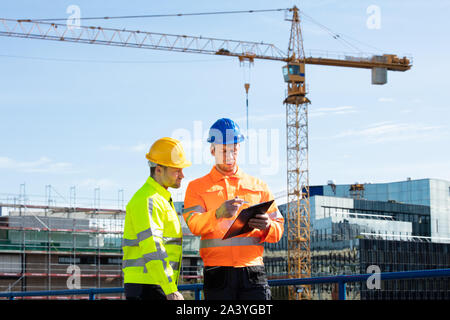 Male Architect Giving Instructions To His Foreman On Clipboard Working At Construction Site Stock Photo