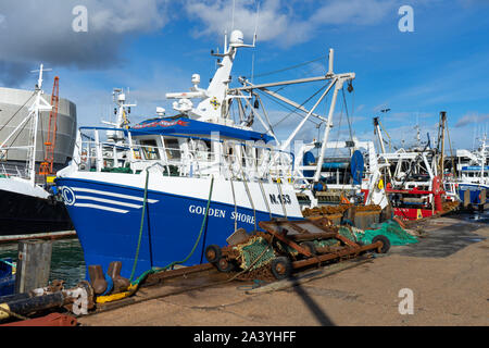 A blue and white fishing trawler tied up on the quayside with fishing nets in front of it Stock Photo
